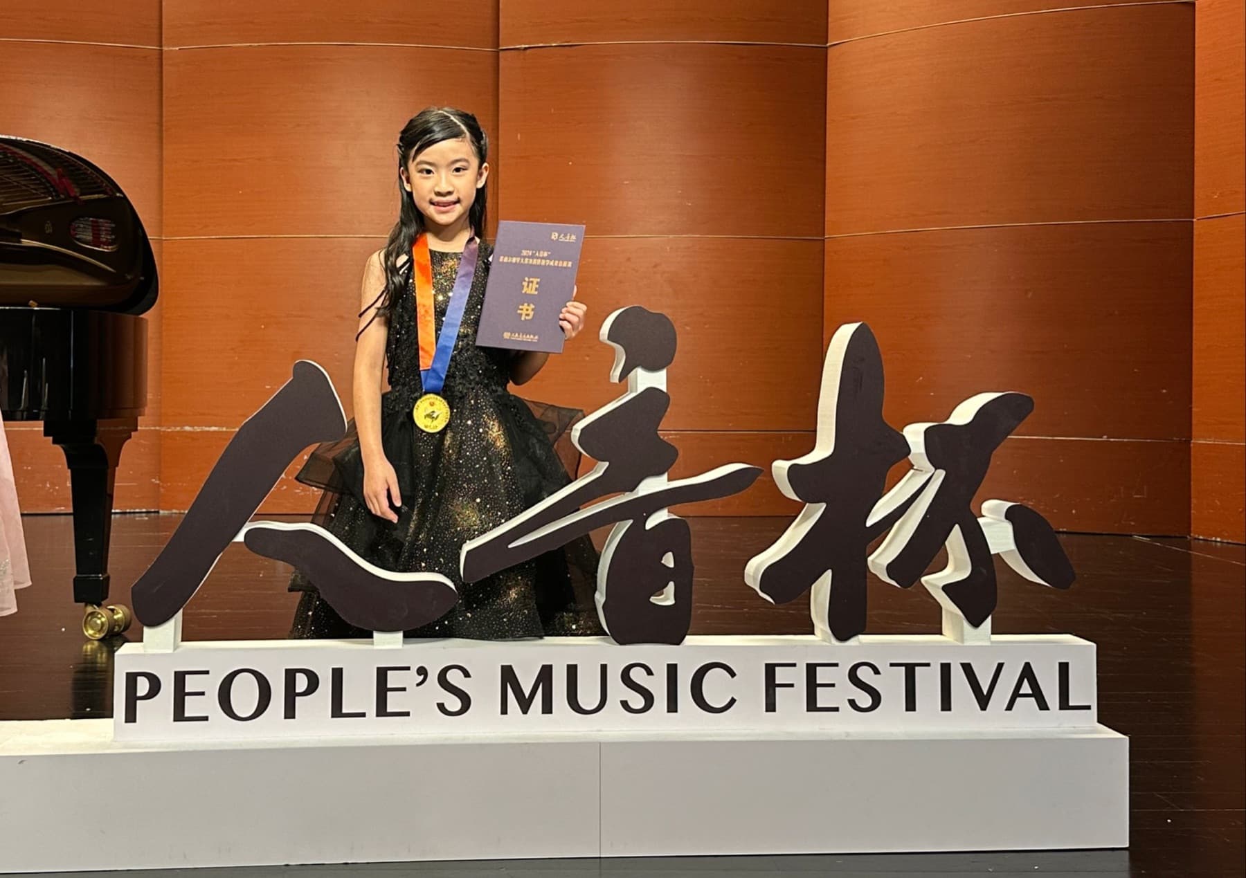 A young pianist holding a certificate and medal on a music festival stage